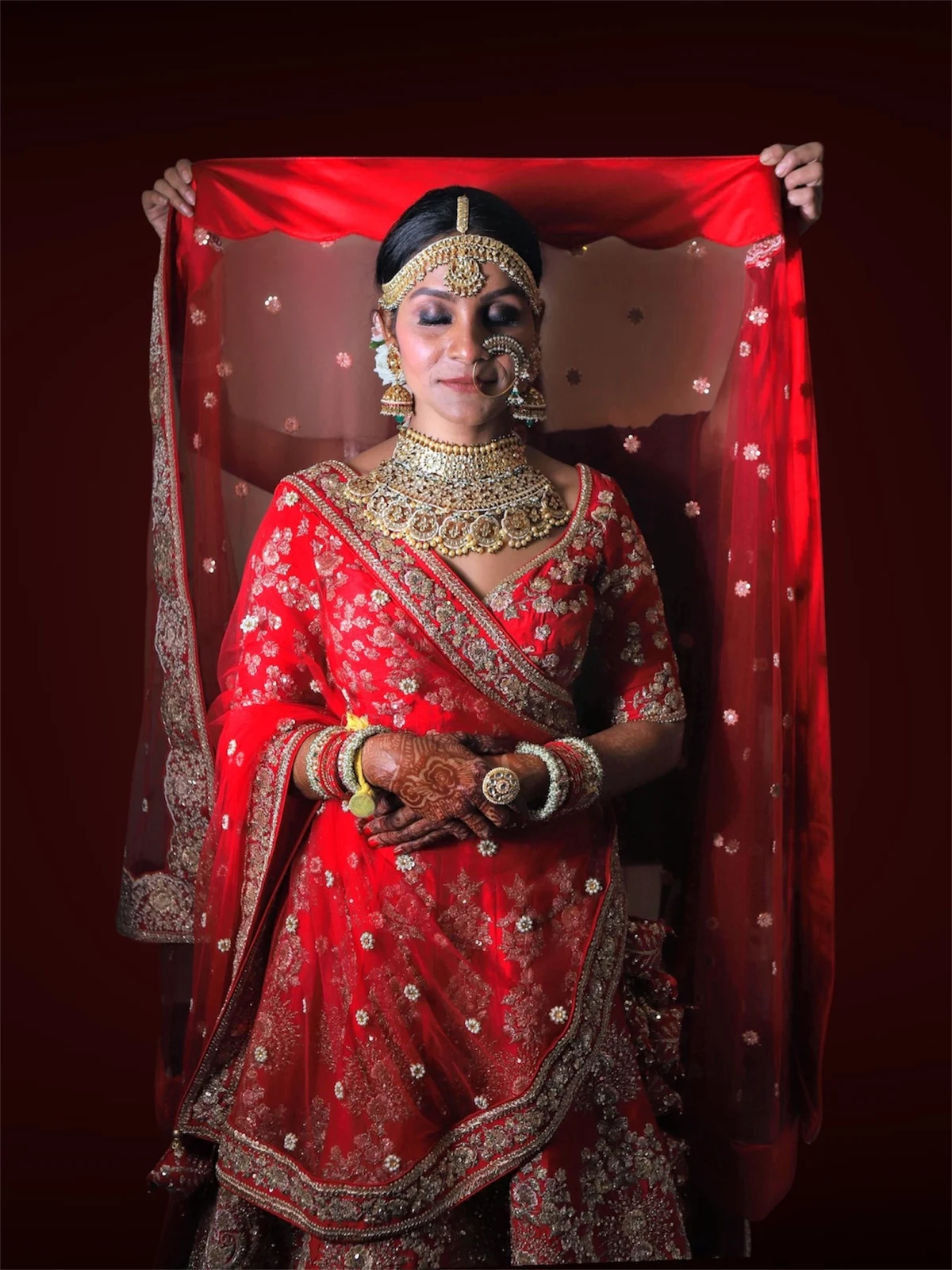 Bridal makeup with defined eyes and a red lip, red bridal attire and a sheer veil.